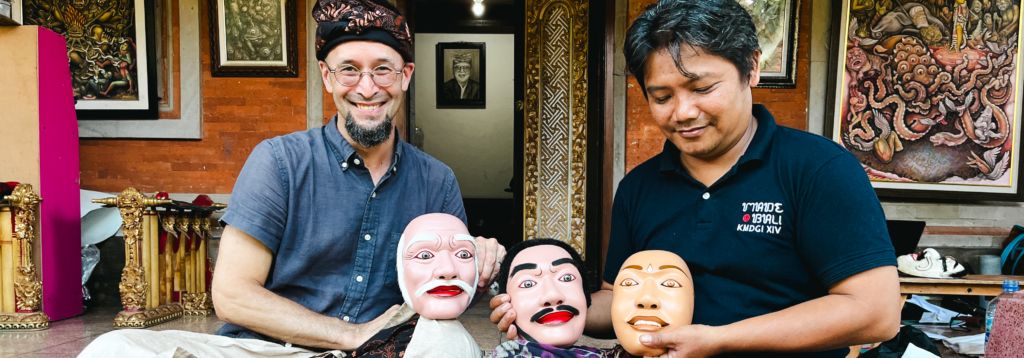 Two men sitting, holding the masks for the performance of Clouds from a Crumbling Giant.